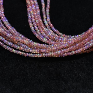 May include: A strand of pink opal beads with iridescent shimmer. The beads are small and round, and they are strung on a clear thread. The beads are arranged in a loose, flowing pattern.