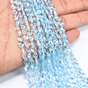 Puede incluir: Una hebra de cuentas de piedras preciosas ovaladas de color azul claro. Las cuentas son facetadas y tienen una apariencia translúcida.