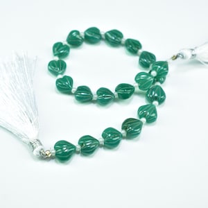 May include: A strand of green heart-shaped beads with white accents and a white tassel. The beads are strung together with small white beads. The tassel is made of white threads and has a silver-colored cap.