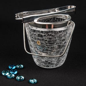 Könnte beinhalten: Ein silberner Eiseimer mit einem Riss-Glas-Design und einer passenden silbernen Eis-Zange. Der Eimer ist mit blauen Glassteinen gefüllt.
