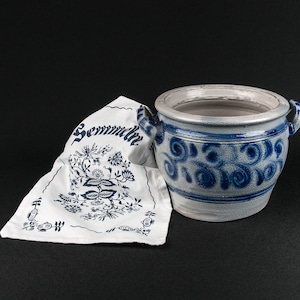 Könnte beinhalten: Ein weißes Tuch mit blauen Blumenmustern und dem aufgedruckten Wort "Semmelknödel" neben einem blauen und weißen Keramiktopf mit Deckel.