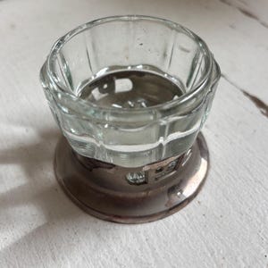 Könnte beinhalten: Ein klarer Salzstreuer aus Glas mit geripptem Design am Rand, auf einem angelaufenen, silberfarbenen Metallsockel. Das kleine, runde Gefäß ist für Salz oder andere Gewürze bestimmt.