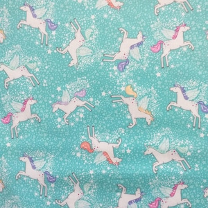 Könnte beinhalten: Ein türkisfarbener Stoff mit einem sich wiederholenden Muster aus weißen Einhörnern mit Flügeln und bunten Mähnen. Die Einhörner fliegen vor einem Hintergrund aus weißen Sternen.