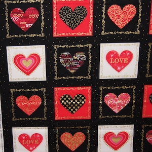 Könnte beinhalten: Schwarzer Stoff mit einem sich wiederholenden Muster aus roten und weißen Quadraten. Jedes Quadrat enthält ein goldenes Herz mit einem anderen Design. Die Herzen haben Muster aus kleinen Herzen, Schnörkeln und Wörtern wie "love" und "be mine".
