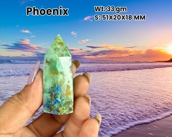 Könnte beinhalten: Ein grüner und blauer Phoenix-Kristallpunkt wird vor einem Strandsonnenuntergangshintergrund gehalten. Der Kristall ist 5,1 cm lang, 2 cm breit und 1,8 cm dick und wiegt 33 Gramm. Das Wort "Phoenix" ist weiß gedruckt.
