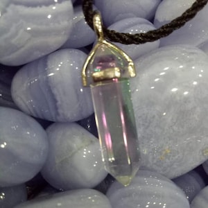 May include: A silver and gold pendant with a clear iridescent crystal point hanging from a black cord. The pendant is surrounded by smooth, light blue stones.