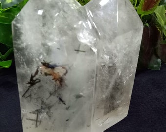 May include: A double-terminated clear quartz crystal with black and brown inclusions. The crystal is polished and has a smooth, glassy surface.