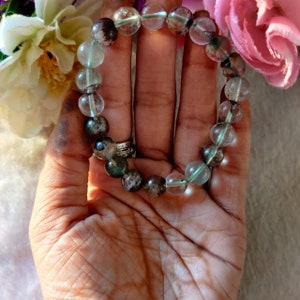 May include: A bracelet made of clear and green gemstone beads. The beads are round and have a speckled pattern.