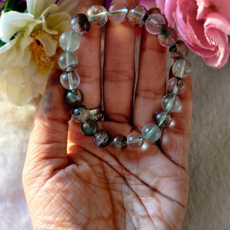 May include: A bracelet made of clear and green gemstone beads. The beads are round and have a speckled pattern.
