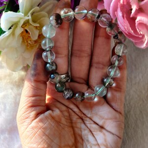 May include: A bracelet made of clear, green, and brown gemstone beads. The beads are round and have a speckled appearance.