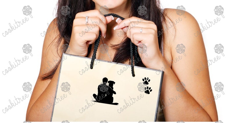 May include: A cream-colored shopping bag with black rope handles. The bag features a black silhouette of a person hugging a dog, along with two sets of black paw prints. The bag is held by a person.