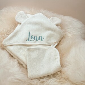 Puede incluir: Toalla con capucha blanca con orejas de oso y un pa&ntilde;o de lavado blanco. La toalla tiene el nombre "Lenn" bordado en color turquesa.