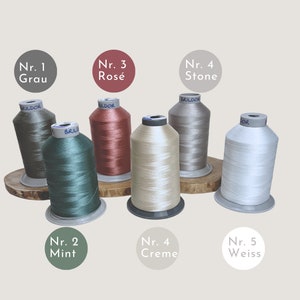 Puede incluir: Cinco carretes de hilo en diferentes colores: verde, rojo, beige, gris y blanco. Los carretes est&aacute;n etiquetados con n&uacute;meros y palabras alemanas para los colores.