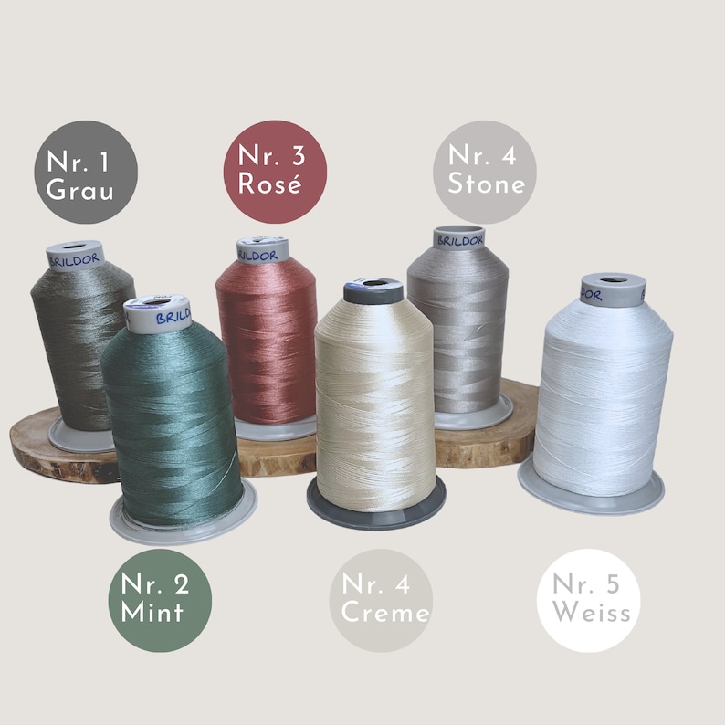 Puede incluir: Cinco carretes de hilo en diferentes colores: verde, rojo, beige, gris y blanco. Los carretes est&aacute;n etiquetados con n&uacute;meros y palabras alemanas para los colores.