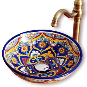 May include: A decorative ceramic sink with a vibrant blue, yellow, and red floral pattern. The sink has a round shape and a brass faucet. The sink's design is reminiscent of traditional Talavera pottery.