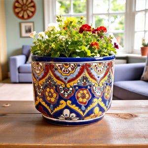 Può includere: Un vaso di fiori in ceramica dipinto a mano con bordo blu e intricati motivi floreali gialli, rossi e bianchi. Il vaso è riempito con una varietà di fiori colorati, tra cui fiori rossi, gialli e bianchi. Il vaso è appoggiato su un tavolo di legno.