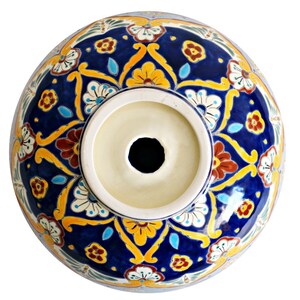 May include: A ceramic sink basin with a vibrant, hand-painted floral design. The basin features a deep blue background adorned with yellow, red, and white floral patterns. The center has a circular opening, and the rim is a light cream color.