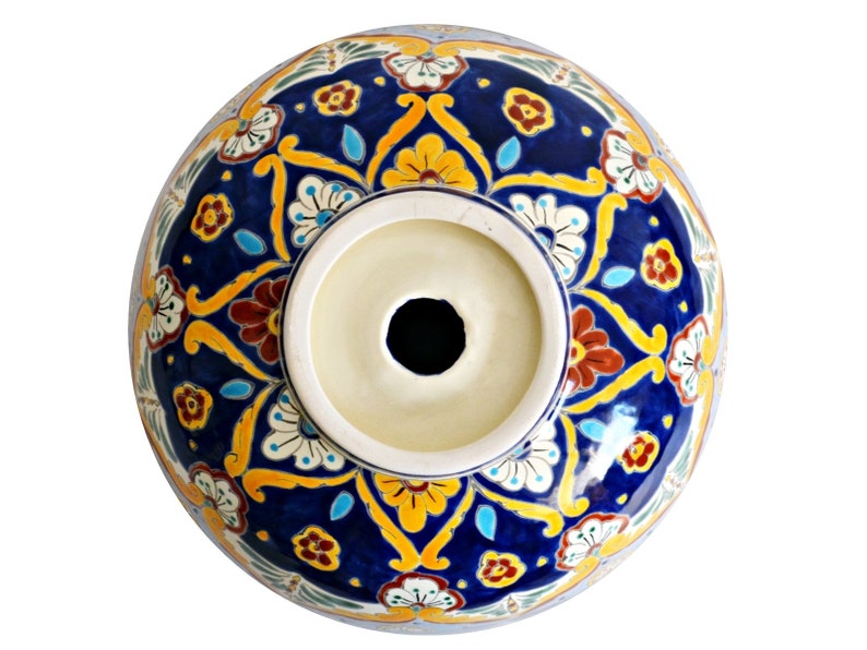 May include: A ceramic sink basin with a vibrant, hand-painted floral design. The basin features a deep blue background adorned with yellow, red, and white floral patterns. The center has a circular opening, and the rim is a light cream color.