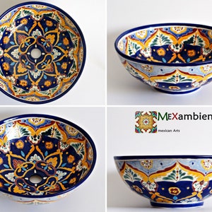May include: Hand-painted ceramic bowl with a vibrant floral design. The bowl features a deep blue rim and interior, with intricate patterns in yellow, orange, and green. The design includes a central hole, likely for a sink or decorative element.