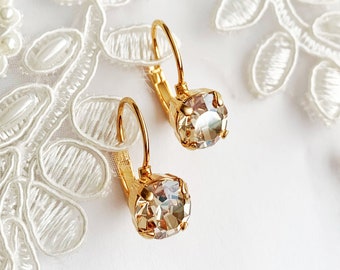 Könnte beinhalten: Ein Paar goldfarbene Ohrhänger mit Klappbügel und runden, facettierten champagnerfarbenen Kristallen in vierzinkigen Metallfassungen. Die Ohrringe haben eine polierte Oberfläche und ein klassisches, hängendes Design.