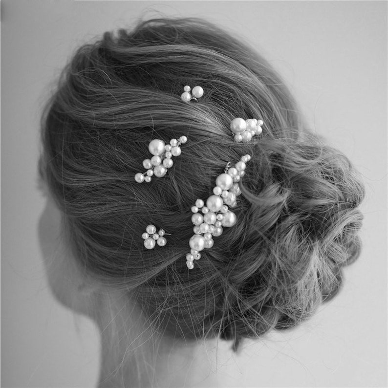May include: A set of pearl hair clips in various sizes and shapes. The clips are arranged in a cluster on a woman's hair.