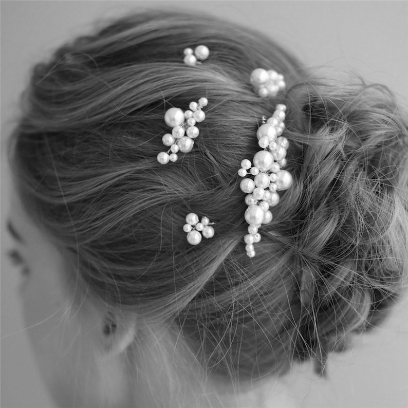 May include: A set of pearl hair clips with different sizes and shapes. The clips are arranged in a cluster on a woman's hair.