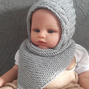 Könnte beinhalten: Eine graue gestrickte Baby-Mütze mit Ohrenklappen und einem passenden Schal. Die Mütze hat ein Zopfmuster.