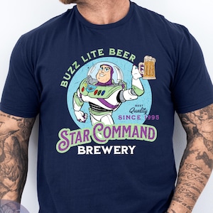 May include: Navy blue t-shirt featuring a cartoon graphic of Buzz Lightyear holding a beer mug. The graphic includes the text "BUZZ LITE BEER" and "STAR COMMAND BREWERY" with "Best Quality Since 1995".
