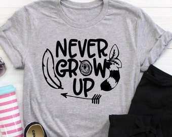 May include: Gray t-shirt with the text "NEVER GROW UP" in black lettering. The text is surrounded by a feather, a leaf, and a raccoon tail.