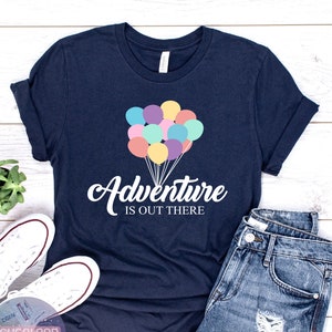 May include: A navy blue t-shirt with a white graphic of colorful balloons and the text "Adventure is out there".