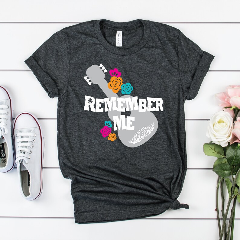 May include: A dark gray t-shirt with a white silhouette of a guitar with floral accents and the text "Remember Me" in white.