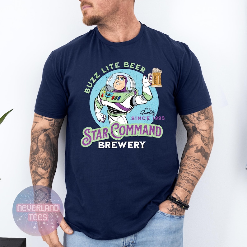 May include: Navy blue t-shirt featuring a cartoon graphic of Buzz Lightyear holding a beer mug. The graphic includes the text "BUZZ LITE BEER" and "STAR COMMAND BREWERY" with "Best Quality Since 1995".