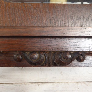 May include: A dark wood clock face with ornate carvings around the edge. The clock face is surrounded by a dark wood frame.