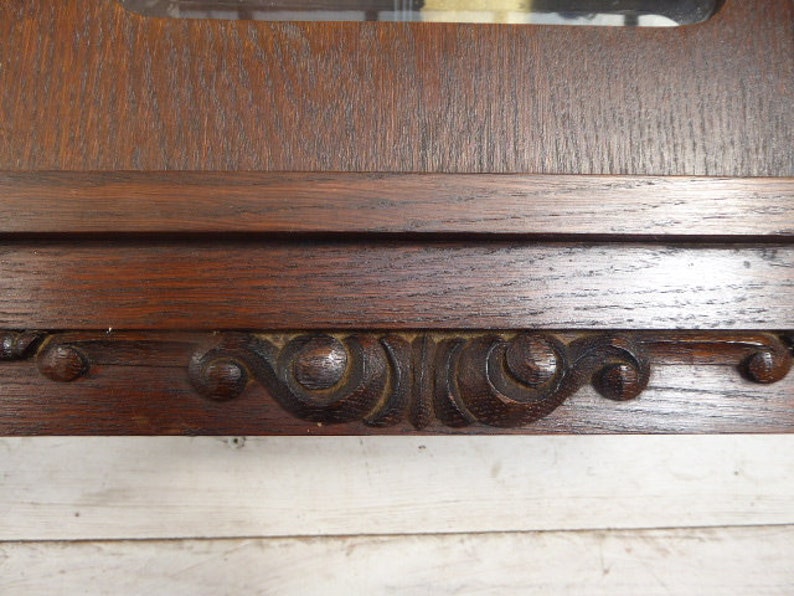 May include: A dark wood clock face with ornate carvings around the edge. The clock face is surrounded by a dark wood frame.