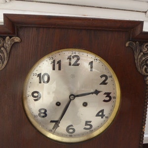 May include: A vintage wooden clock with a round, white face and black hands. The clock has a decorative, ornate design around the edge of the face and a dark wood frame.