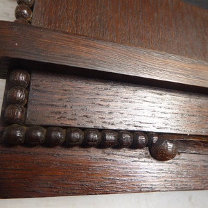 May include: Close-up of a dark brown wooden frame with a beaded trim. The frame has a smooth, polished finish and a slightly raised edge.