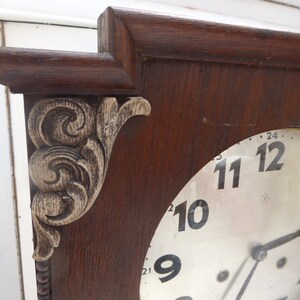 May include: A vintage wooden clock with a white face and black Roman numeral hour markers. The clock has a decorative carved wooden frame with a floral design.