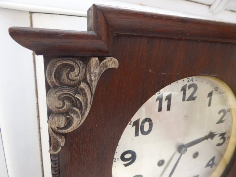 May include: A vintage wooden clock with a white face and black Roman numeral hour markers. The clock has a decorative carved wooden frame with a floral design.