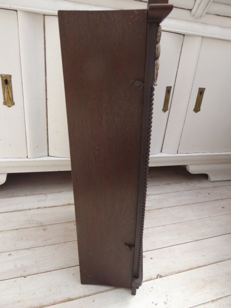 May include: A dark brown wooden wall mounted cabinet with intricate carvings and a beaded trim. The cabinet has a single door and is closed.