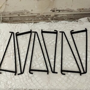 May include: A set of eight black metal shelf brackets. The brackets are in the shape of a triangle and have a simple, industrial design.
