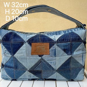 May include: A denim handbag with a geometric patchwork design. The bag is 32cm wide, 20cm high, and 10cm deep. It features a brown leather patch and a denim handle.