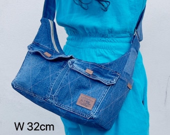 May include: A blue denim shoulder bag with a zip and two front pockets. The bag has a brown label and measures 32cm wide, 16-26cm high, and 5-12cm deep.