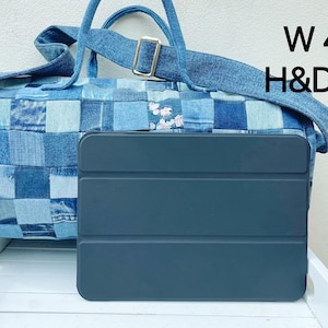Op de afbeelding: Een blauwe denim patchwork tote bag met een zwarte tablet hoes. De tas is 42 cm breed en 20 cm hoog en diep.