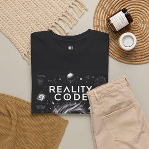 Könnte beinhalten: Ein schwarzes T-Shirt mit dem weißen Schriftzug REALITY CODE mittig auf der Brust. Die Grafik zeigt wissenschaftliche Gleichungen, eine Spiralgalaxie, einen Planeten und ein geometrisches Kugeldesign in Weiß auf dem schwarzen Stoff.
