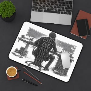 Könnte beinhalten: Eine rechteckige Schreibtischunterlage mit einer schwarz-weißen Illustration einer Person, die an einem Schreibtisch mit mehreren Monitoren sitzt. Die Person sitzt mit dem Rücken zum Betrachter und ihre Kleidung besteht aus dem Text, The build must go on.