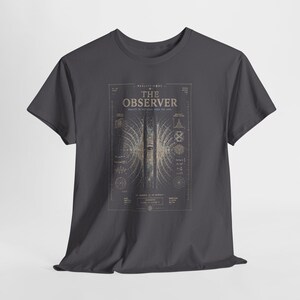 May include: A charcoal grey t-shirt featuring a graphic print titled THE OBSERVER. The design includes a central human eye surrounded by radiating light patterns, mathematical formulas, and technical diagrams in a light beige and white colour palette.