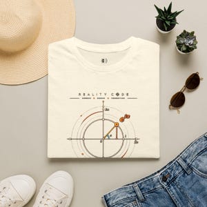 Op de afbeelding: Een crèmekleurig t-shirt met een afbeelding van de formule van Euler, e^ix, op een assenstelsel van het complexe vlak. Het ontwerp bevat de tekst "REALITY CODE" boven het wiskundige diagram, dat oranje en zwarte lijnen gebruikt.