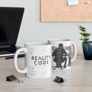 Könnte beinhalten: Ein weißer Keramikbecher mit dem schwarzen Text REALITY CODE, Programmiersyntax und einer detaillierten Illustration einer Person an einem Schreibtisch mit dem Text The build must go on. Das Design enthält technische Code-Schnipsel.