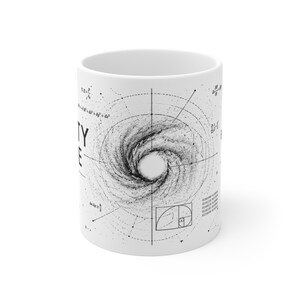 May include: A white ceramic mug featuring a black and white graphic of a spiral galaxy centered within geometric lines and mathematical equations. The design includes the text TY and E on the left side, along with a golden ratio spiral box.