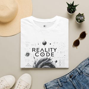 Op de afbeelding: Een wit t-shirt met een zwarte grafische print met de tekst REALITY CODE. Het ontwerp bevat wetenschappelijke symbolen, wiskundige vergelijkingen, een spiraalstelsel, een DNA-streng en planetaire illustraties op het borstgedeelte.